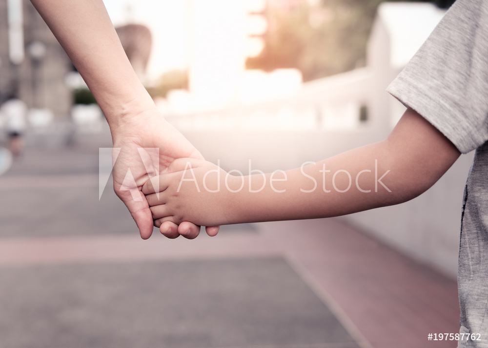 A parent holds the hand of a small boy in the sunset.